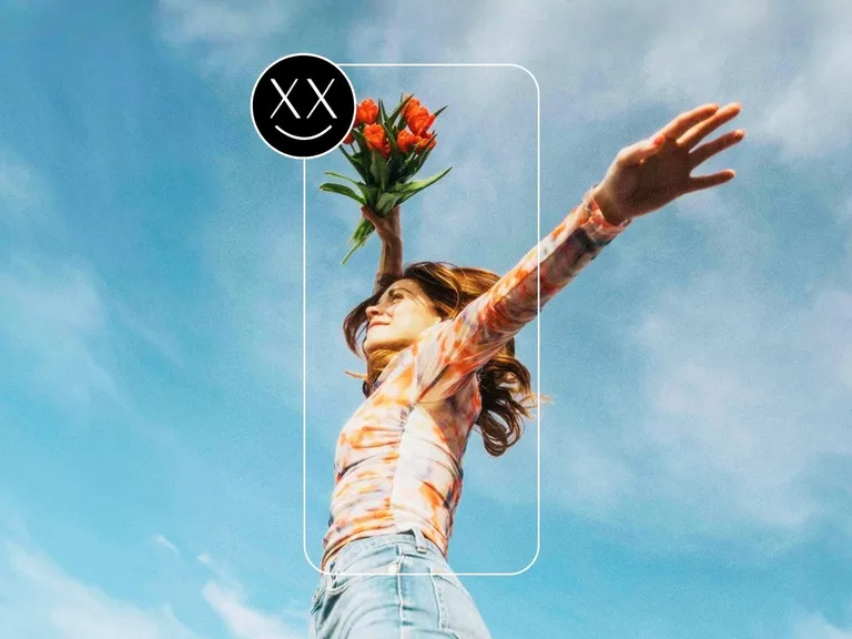 A woman with outstretched arms holding flowers against the sky, framed by a smartphone, symbolizing financial independence & wealth building for women