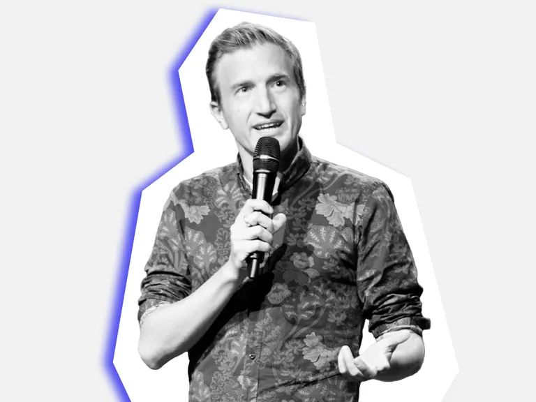 Comedian Stefan Büsser hält ein Mikrofon und spricht.